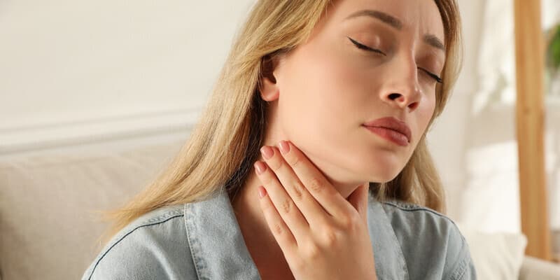 Suchość w jamie ustnej i w gardle – przyczyny, metody zapobiegania. Kobieta dotyka dłonią szyi.